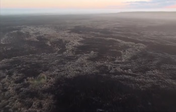 Vista aérea de un vasto terreno afectado por un incendio, con parches de vegetación quemada y algunos pastizales intactos bajo un cielo brumoso
