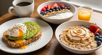 Vista aérea de una mesa de madera con un desayuno variado: tostada de aguacate, yogur con bayas, porridge de avena, café y zumo de naranja.