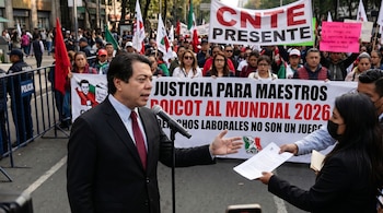 Mario Delgado de Morena en un micrófono, recibiendo documentos de una persona, con una multitud y pancartas de la CNTE durante una protesta.