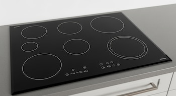 Vista en ángulo superior de una placa de inducción negra de cinco zonas sobre una encimera gris, con controles táctiles y círculos blancos distintivos.