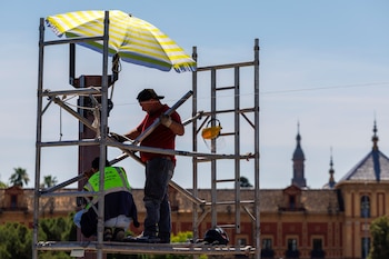 Dos trabajadores se protegen del sol en el puente de San Telmo en Sevilla a 28 de mayo de 2026. (EFE/ Julio Muñoz)