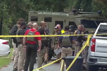 Chalecos tácticos con inscripciones U.S. Marshals y Police, agentes de seguridad, vehículo blindado, cinta amarilla, camioneta, árboles