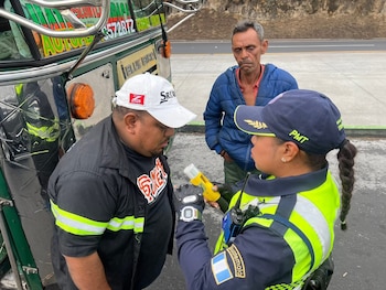 Una agente de policía con chaleco reflectante realiza una prueba de alcoholemia a un hombre cerca de un autobús. Otro hombre observa en segundo plano