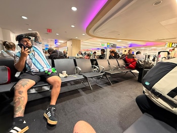 Un hombre con camiseta argentina sentado junto a la misma fila de bancas que el hermano del arquero de la selección española David Raya