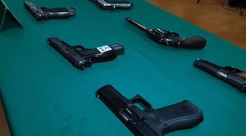 Diferentes tipos de pistolas y un revólver colocados sobre una mesa cubierta con un mantel verde