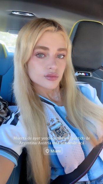 Mujer rubia sentada en el asiento de un coche. Viste la camiseta de la selección argentina de fútbol. La imagen contiene texto que menciona su ubicación en Miami