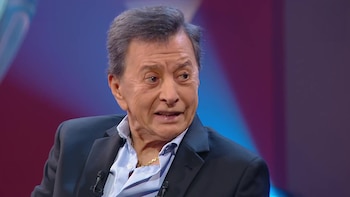 Retrato de Palito Ortega vistiendo saco oscuro y camisa azul, en un estudio con luces de fondo