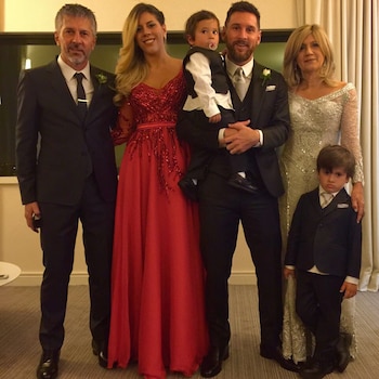 Lionel Messi, Antonela Roccuzzo, Jorge Messi y Celia Cuccittini sonríen en un evento festivo con luces azules y un cartel 'Campeones del Mundo' de fondo