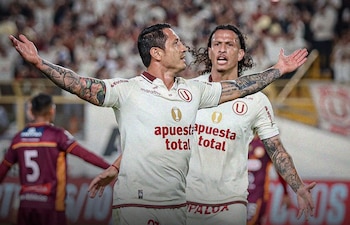 Dos futbolistas del club Universitario de Deportes celebran con los brazos abiertos sobre el terreno de juego frente a la tribuna