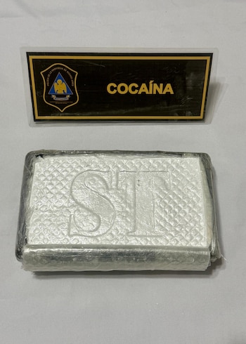 Bloque rectangular blanco envuelto en plástico con letras STI. Un cartel negro con el escudo de la Policía de la Provincia de Buenos Aires y la palabra "COCAÍNA"