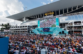 Una gran multitud de aficionados frente al Hard Rock Stadium y una pantalla gigante que muestra imágenes de una carrera de Fórmula 1
