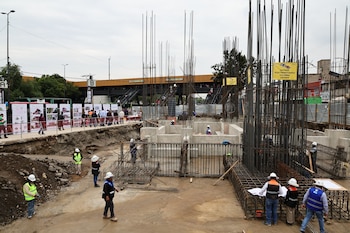 Trabajadores con cascos y chalecos reflectantes en una excavación con estructuras de varillas de acero y columnas de concreto