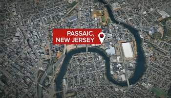 Mapa satelital de una ciudad con edificaciones, calles y un río. Un rótulo rojo indica PASSAIC, NEW JERSEY, con un marcador de posición blanco