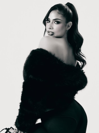 Imagen en blanco y negro de Daniela Celis posando de espaldas, mirando por encima del hombro. Viste una chaqueta de piel sintética negra sobre los hombros