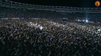 Vista aérea de un estadio lleno con una inmensa multitud de personas en un concierto nocturno. Las luces del escenario brillan al fondo