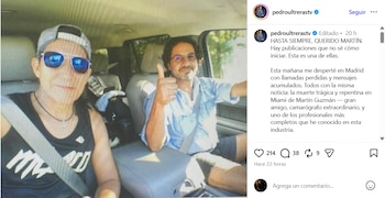 Dos hombres en un coche, uno con gorra y gafas de sol, el otro con camisa clara y barba, haciendo un pulgar arriba, ambos sonriendo a la cámara