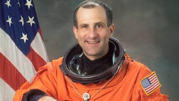 Donald Pettit sonríe con un traje espacial naranja ante la bandera de Estados Unidos