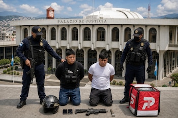 Dos hombres de rodillas y dos policías de pie frente al Palacio de Justicia, con un arma, teléfonos y una mochila de reparto en el suelo.
