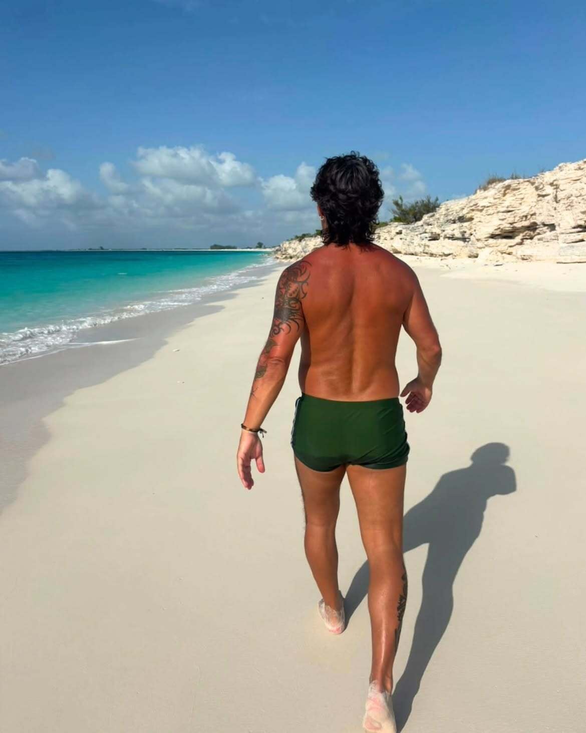 Diego Torres, de espaldas y sin remera, recorre la orilla de una playa de arena blanca. Su tatuaje de trazos negros, que le cubre el brazo derecho, es visible en el perfil