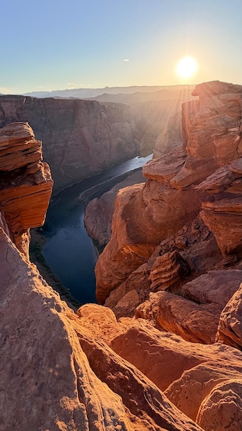 Cañón de rocas rojizas con un río en el fondo y el sol brillante en un cielo claro