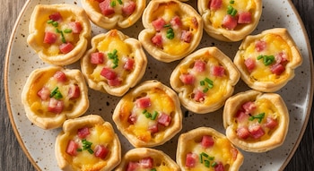 Varias canastitas de masa dorada con relleno de queso fundido, dados de jamón y cebollino picado, dispuestas en un plato redondo.