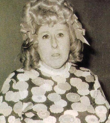 Retrato de primer plano de Nelly Lainez, una mujer de cabello rizado con lazos y un vestido estampado, mirando al frente con expresión neutra