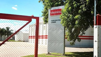 Vista exterior de la planta industrial de Lácteos Verónica en Lehmann, con un cartel identificativo, reja roja y edificios blancos con franjas rojas bajo cielo azul