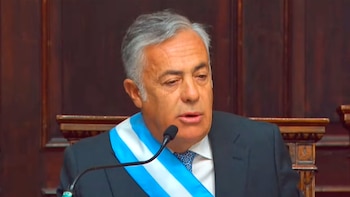 Primer plano de Alfredo Cornejo, un hombre de mediana edad con cabello gris, traje oscuro y banda presidencial, hablando frente a un micrófono. Fondo de madera