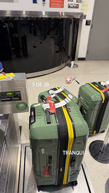 Varias valijas verdes en báscula de aeropuerto. Display digital muestra 28.0. Etiquetas, correas amarillas y texto '3 DE 28'. Emoji de cerdo