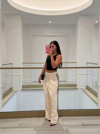 Antonela Roccuzzo se toma una autofoto frente al espejo vistiendo un top negro, pantalón holgado claro y sosteniendo un teléfono rosa