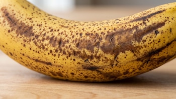 Vista de cerca de la cáscara amarilla con pecas marrones de un plátano sobre una superficie de madera