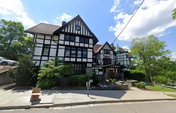 Fachada de un edificio de estilo tudor con entramado de madera en blanco y negro, junto a una acera con vegetación y cielo azul