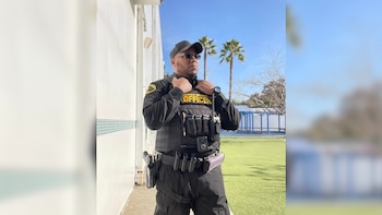 Amin Abdullah, un hombre con gafas y gorra, de pie y mirando al frente, vestido con un uniforme de guardia de seguridad y un chaleco táctico