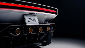 Vista trasera de un automóvil de color claro con la placa RDSTR, una tira de luz roja y varios tubos circulares en el difusor posterior