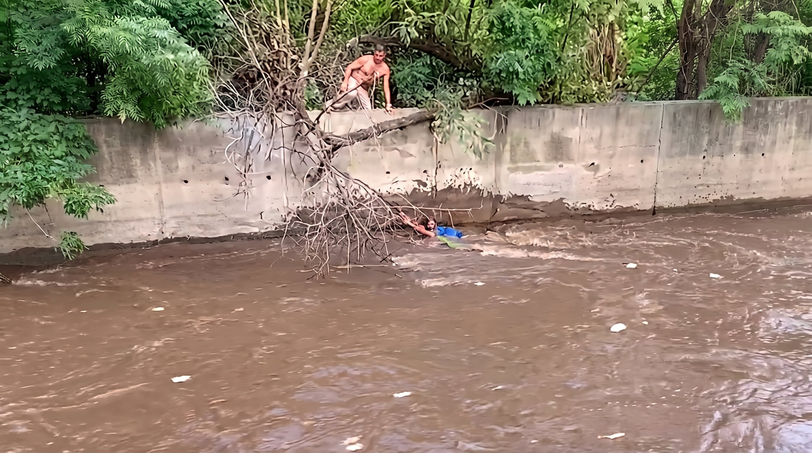 Un hombre intenta auxiliar a una persona atrapada en la corriente de un cauce en Nicaragua mientras esta se sujeta a la rama de un árbol. (Imagen Ilustrativa Infobae)