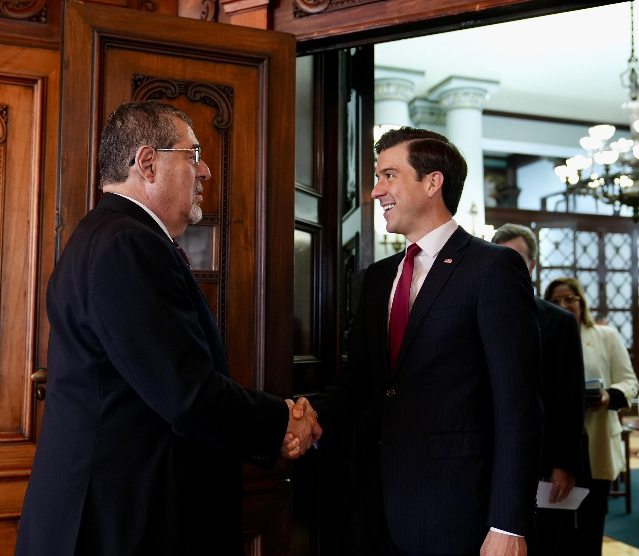 Cuatro funcionarios sonríen mientras participan en una productiva reunión diplomática en un entorno formal, con las banderas de Guatemala y Estados Unidos visibles sobre una mesa auxiliar. (Embajada de Estados Unidos en Guatemala)