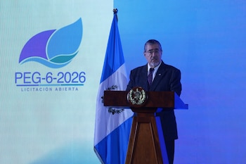 Dos hombres en traje sentados ante una mesa con micrófonos y una pantalla azul que muestra el logotipo de la licitación PEG-6-2026
