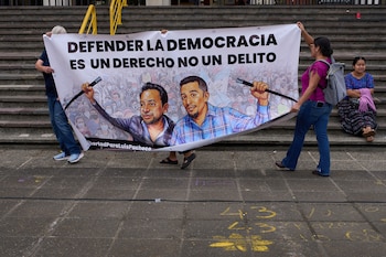 ARCHIVO - Activistas portan una pancarta que dice "Defender la democracia es un derecho no un delito" sobre retratos de los líderes indígenas encarcelados Luis Pacheco (izquierda) y Héctor Chaclán, quienes enfrentan cargos de terrorismo y asociación ilícita en relación con las protestas nacionales de 2023, frente a la Corte Suprema en Ciudad de Guatemala, el 25 de agosto de 2025. (Foto AP/Moisés Castillo, Archivo)