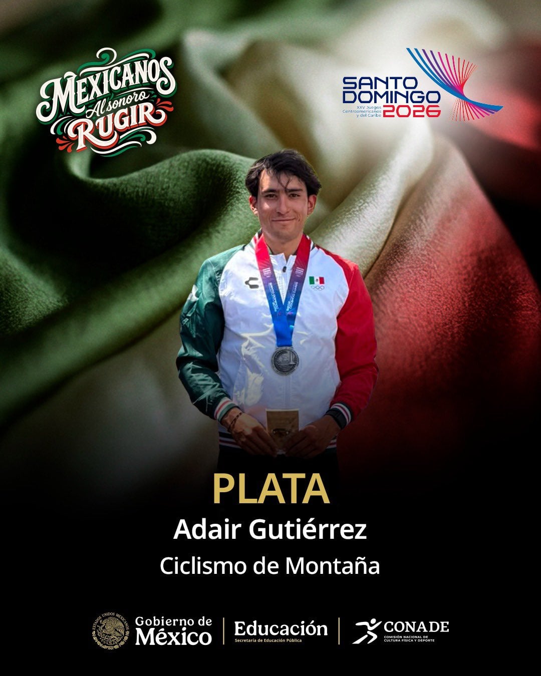 El ciclista mexicano Adair Gutiérrez sonríe con su medalla de plata y una placa de reconocimiento por su desempeño en ciclismo de montaña para los Juegos Santo Domingo 2026. ( X / CONADE)