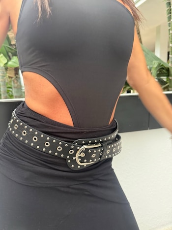 Vista cercana del torso de una mujer con un traje de baño o body negro con aberturas laterales y un cinturón negro con remaches plateados