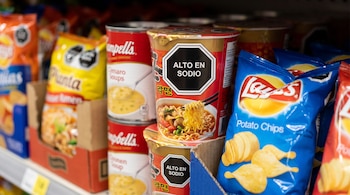 Bolsas de papas fritas, latas de sopa y vasos de fideos instantáneos con sellos octagonales de advertencia en un estante.
