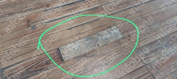 Piso de madera compuesto por tablas largas. Una tabla central de color más claro y textura irregular está rodeada por un círculo verde