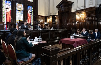 alumnos en bancos de madera frente a un estrado judicial, pantallas de video y un vitral en una sala con paredes de madera