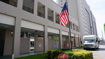 Edificio moderno de múltiples pisos con locales comerciales en la planta baja, una bandera estadounidense ondeando y un autobús blanco estacionado al frente