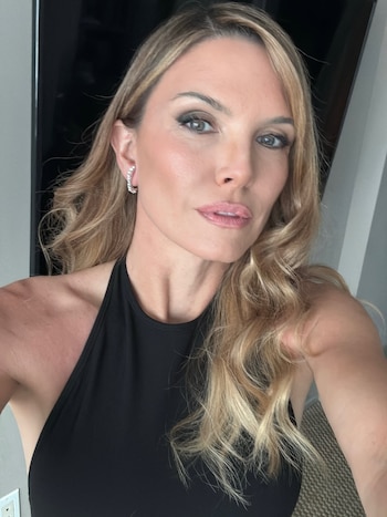 Retrato de una mujer con cabello rubio ondulado, aretes de argolla plateados y un top negro de cuello halter, mirando al frente