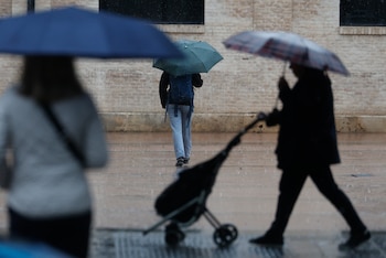 Varias personas se protegen de la lluvia, este sábado en Valencia. (EFE/Kai Forsterling)