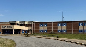 Edificio de Graves County Middle School con fachada de ladrillo, entrada principal, ventanales con letras azules, pasto verde y camino de asfalto