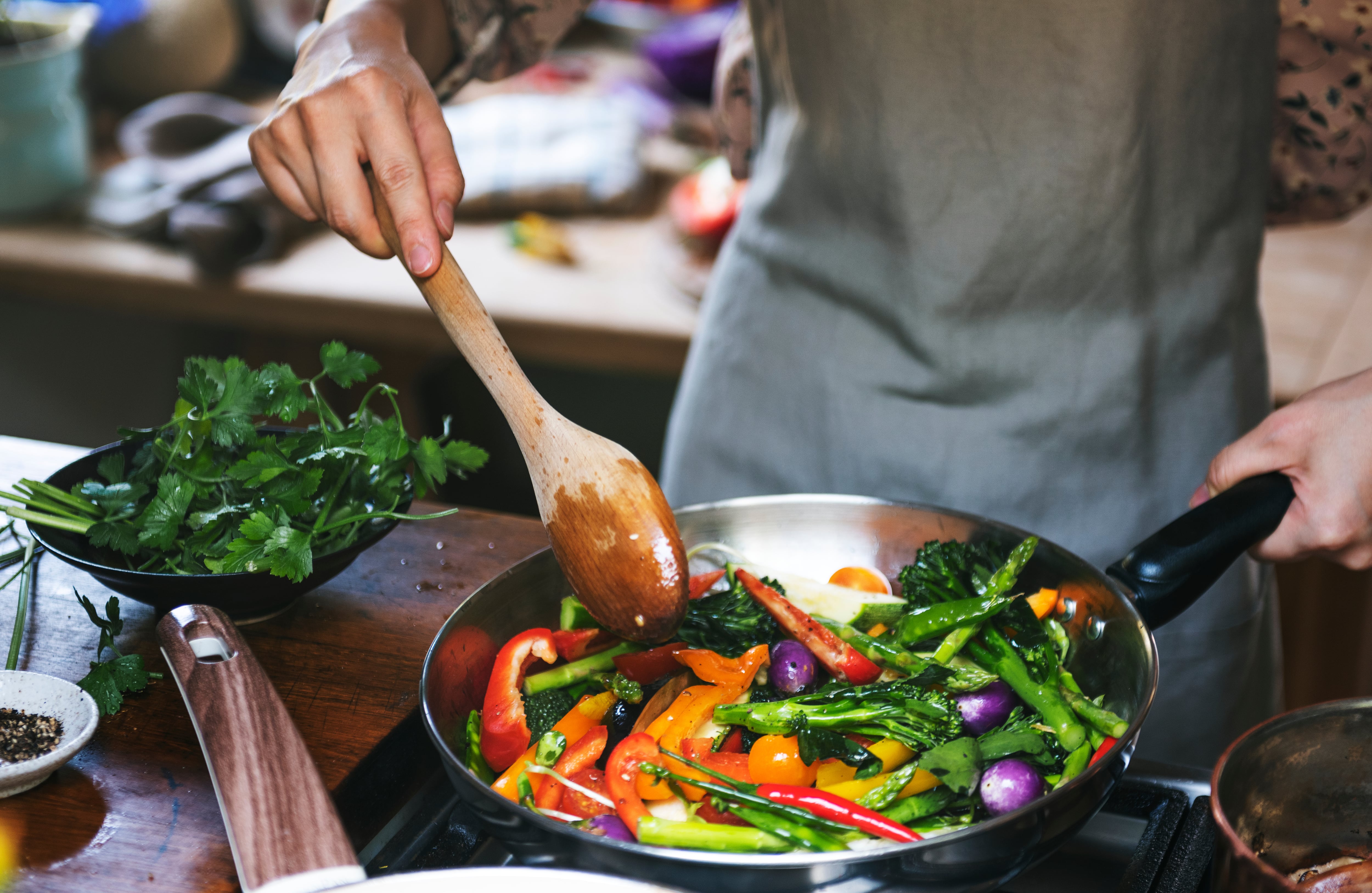 Un hombre cocinando verduras en una sartén (AdobeStock)