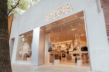 Fachada de la tienda Isadora con grandes ventanas de exhibición, mostrando bolsos y accesorios. Un árbol frondoso es visible a la izquierda