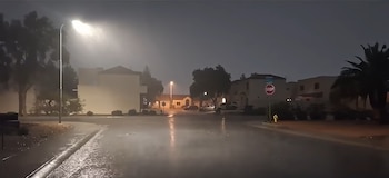 Calle residencial durante la noche con asfalto mojado, lluvia intensa bajo el alumbrado público, casas y una señal de alto